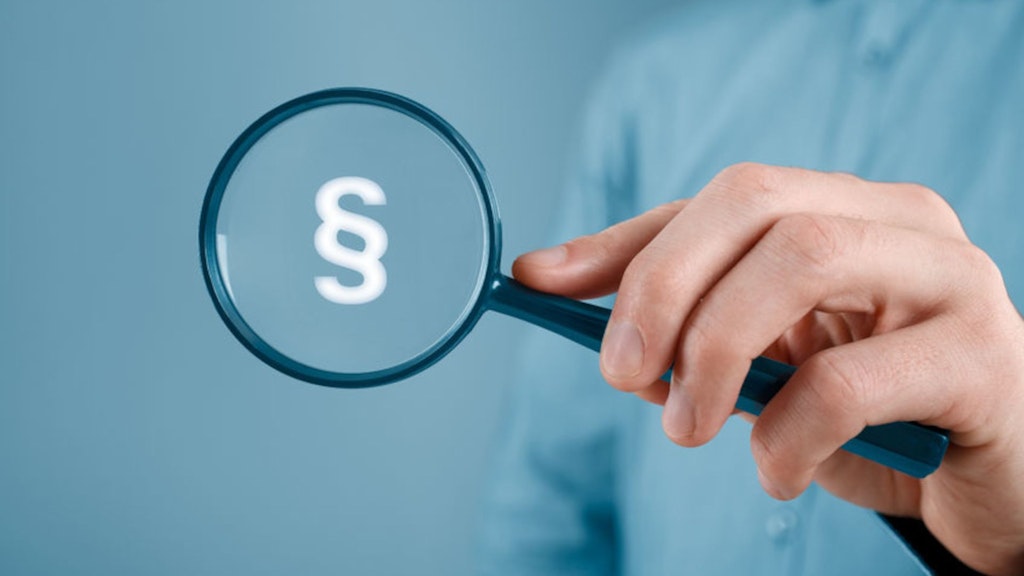 Eine Hand hält eine schwarze Lupe und darin wird das Paragraphenzeichen sichtbar.