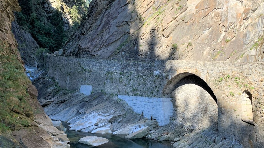 Un vieux pont en pierre s'étend sur une étroite gorge aux parois rocheuses abruptes.  