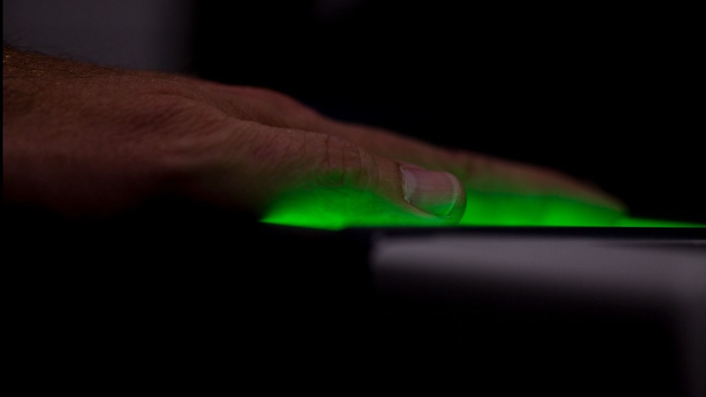Eine Hand wird auf einem Scanner mit grünem Licht gescannt. Der Fokus liegt auf den Fingern und dem leuchtenden Licht.