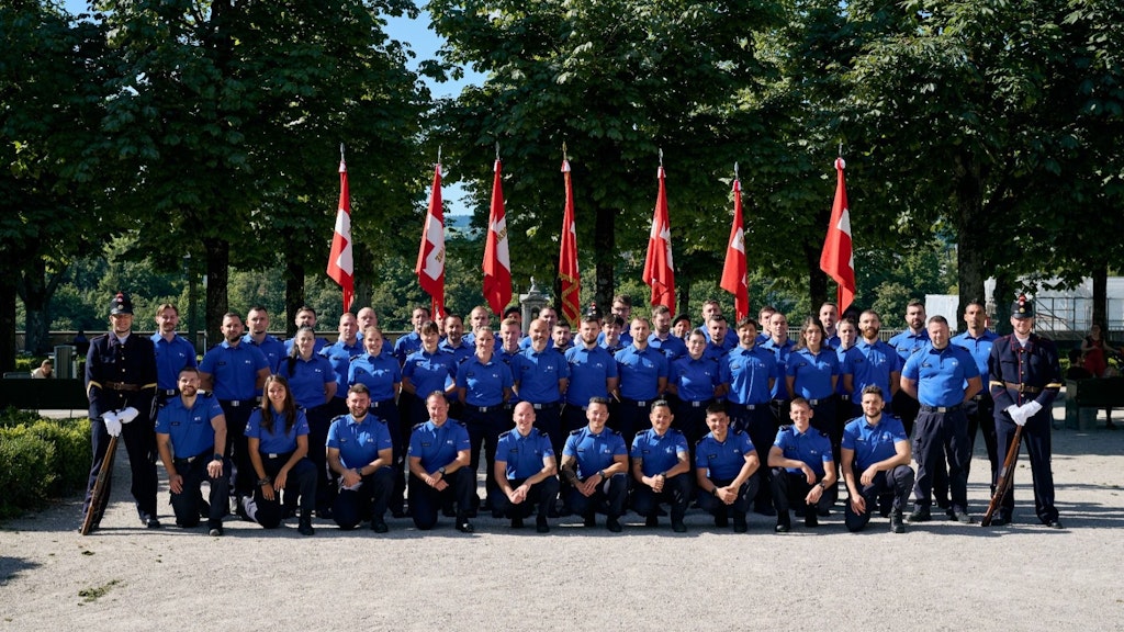 Photo de groupe des collègues nouvellement assermentés dans un parc, devant 7 drapeaux suisses.