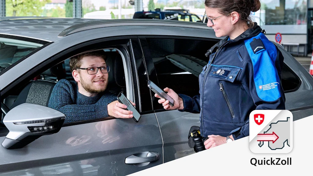 Eine Zollmitarbeiterin überprüft die Dokumente eines Autofahrers mit einer App. Beide halten Smartphones in der Hand.