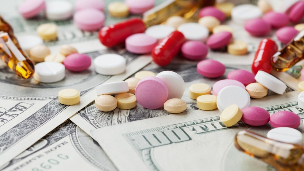 Various colorful tablets and capsules are lying on several hundred-dollar bills.