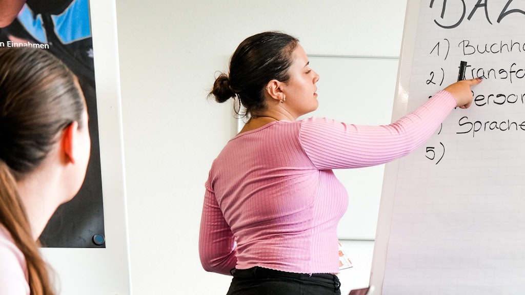 Eine Frau präsentiert während eines Workshops und zeigt auf ein Flipchart.