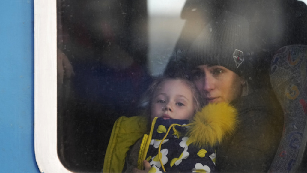 Eine Frau und ein Kind sitzen in einem Zug und schauen aus dem Fenster. Das Kind trägt eine Jacke mit gelbem Fellkragen. Die Szene wirkt nachdenklich und ruhig.