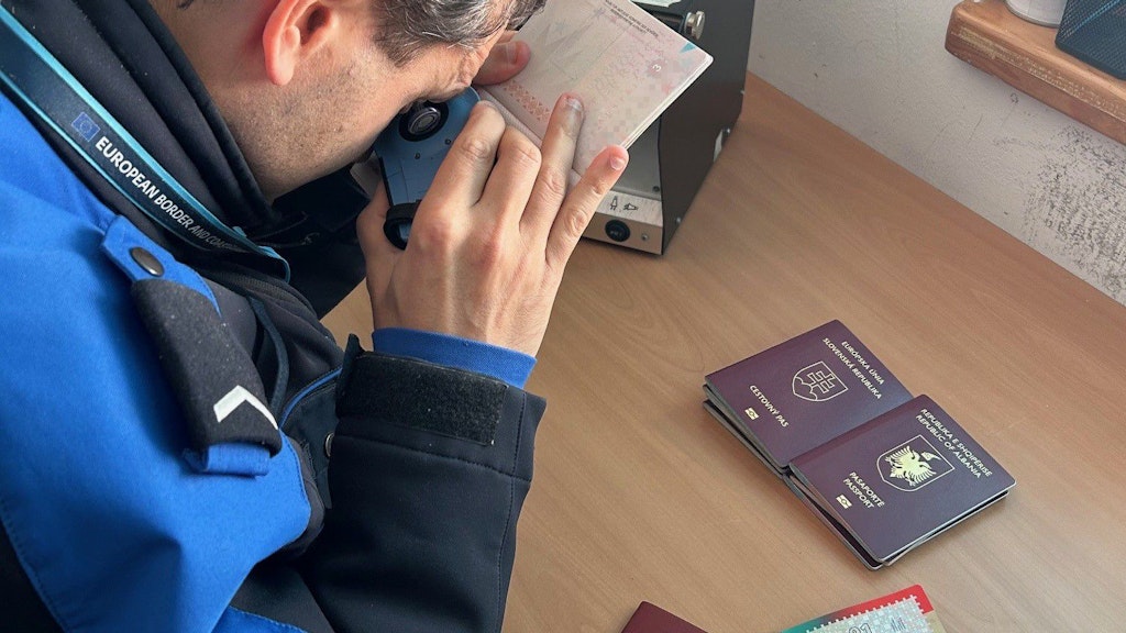 Un agent des douanes et des frontieres verifie l authenticite d un passeport a l aide d un appareil sur un bureau. Devant lui se trouvent plusieurs passeports et documents.  
