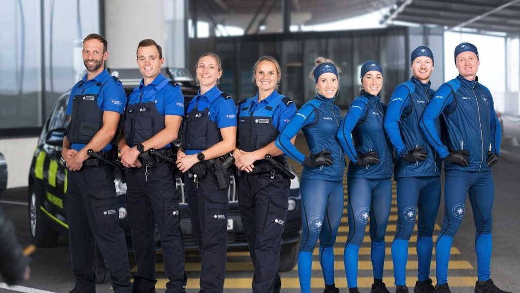 Neun Mitarbeitende des Schweizer Zolls und der Grenzsicherheit stehen in Uniform und Sportbekleidung nebeneinander. Im Hintergrund ist ein Einsatzfahrzeug zu sehen.