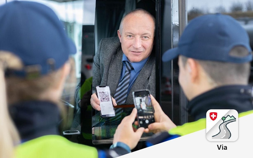  Ein Mann in einem Anzug zeigt einen QR-Code auf seinem Smartphone durch ein Fahrzeugfenster. Zwei Personen in Uniform scannen den Code mit einem anderen Smartphone.