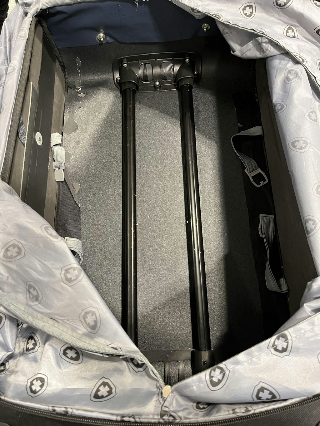 Offener Koffer zeigt den Innenraum mit zwei schwarzen Teleskopgriffen und grauem Innenfutter mit Muster.
