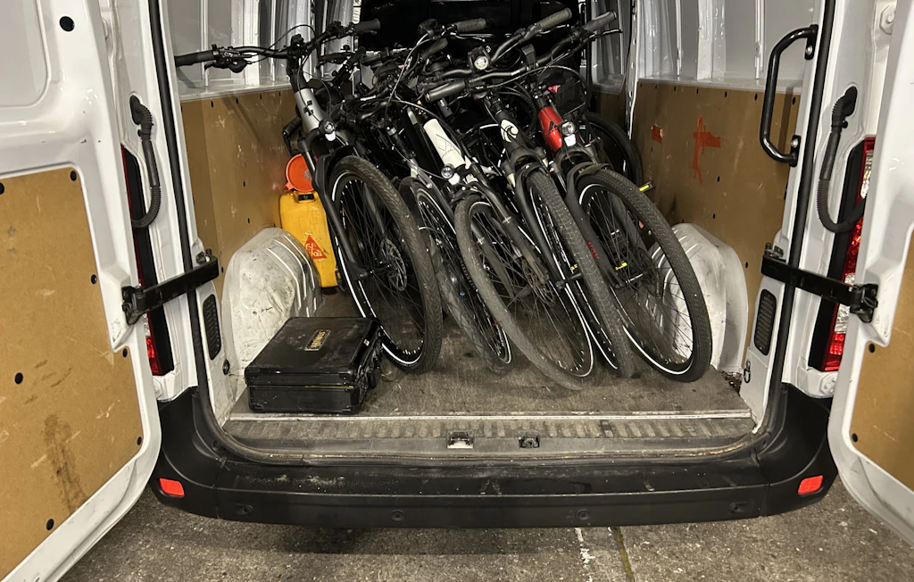 Im Laderaum eines weissen Lieferwagens stehen mehrere Fahrräder nebeneinander. Die Fahrräder sind ordentlich aufgestellt, daneben befindet sich eine schwarze Kiste und ein gelber Kanister.  