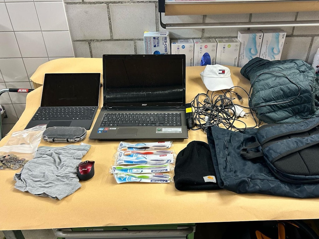 Verschiedene Gegenstände, darunter zwei Laptops, Zahnbürsten, eine Mütze und Kabel, liegen auf einem Tisch. Diese Objekte könnten mutmassliches Diebesgut sein.