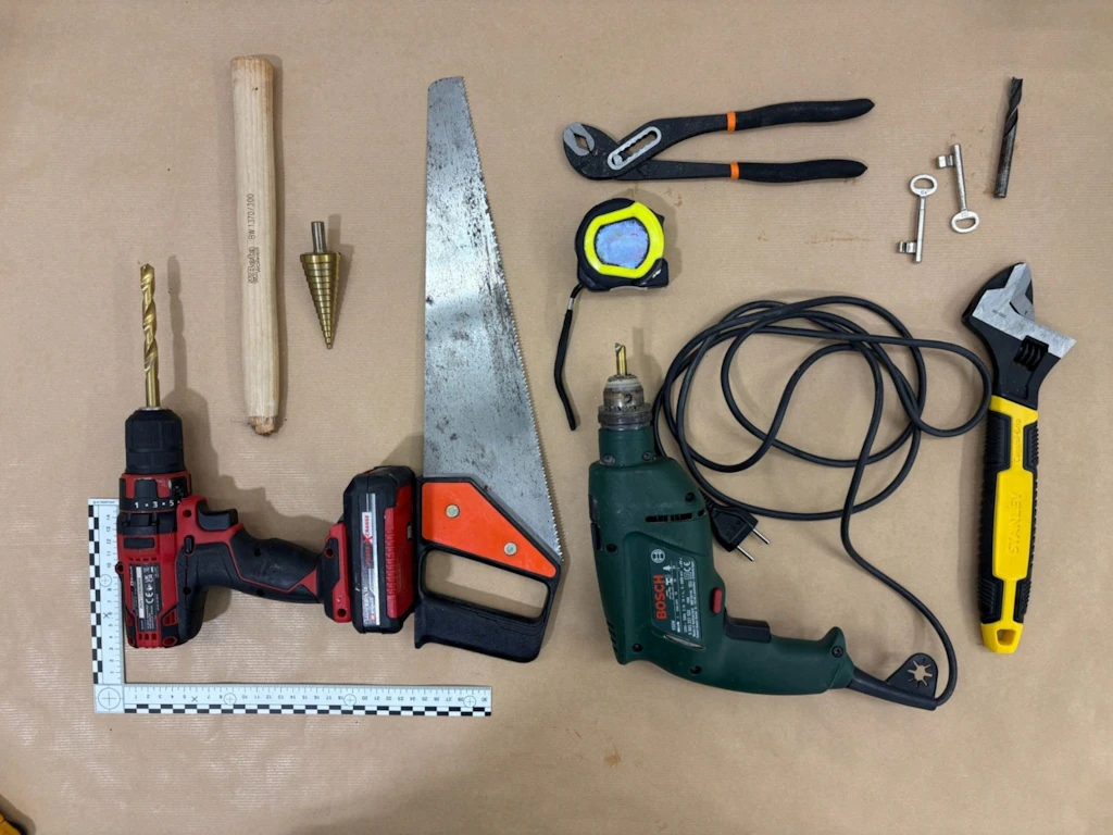Verschiedene Werkzeuge wie Bohrmaschine, Akkuschrauber, Säge, Zange, Massband, Schlüssel und Schraubenschlüssel liegen auf einer hellen Unterlage. Die Gegenstände wurden im Rahmen einer Zollkontrolle sichergestellt und stehen im Zusammenhang mit einem Einbruchdiebstahl.  