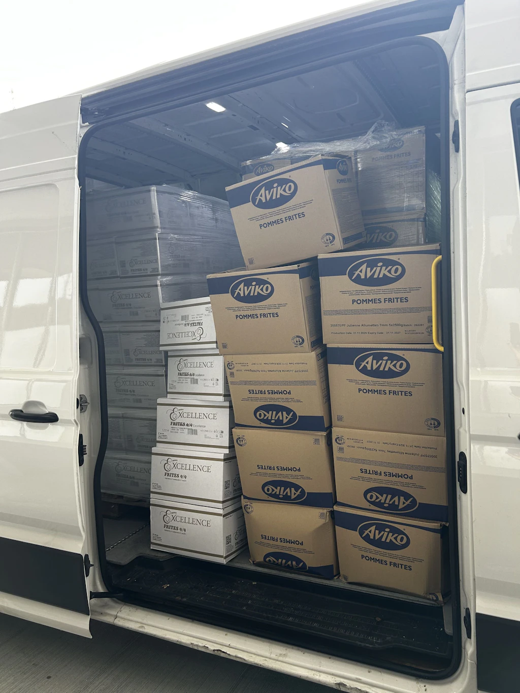 Ein Lieferwagen ist geöffnet und zeigt zahlreiche Kartons mit Pommes Frites der Marken Aviko und Excellence. Die Kartons sind ordentlich gestapelt und nehmen den gesamten Laderaum des Fahrzeugs ein.