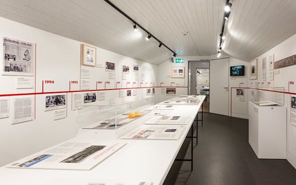 Eine Ausstellung im Schweizer Zollmuseum zeigt Dokumente und Bilder zur Geschichte des Zollvertrags zwischen der Schweiz und Liechtenstein. Die Ausstellung ist in einem hellen Raum mit weißen Wänden und einer Zeitleiste an der Wand.