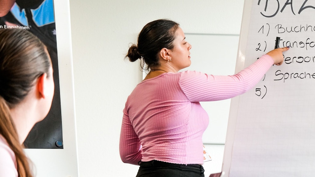 Eine Frau präsentiert während eines Workshops und zeigt auf ein Flipchart.  