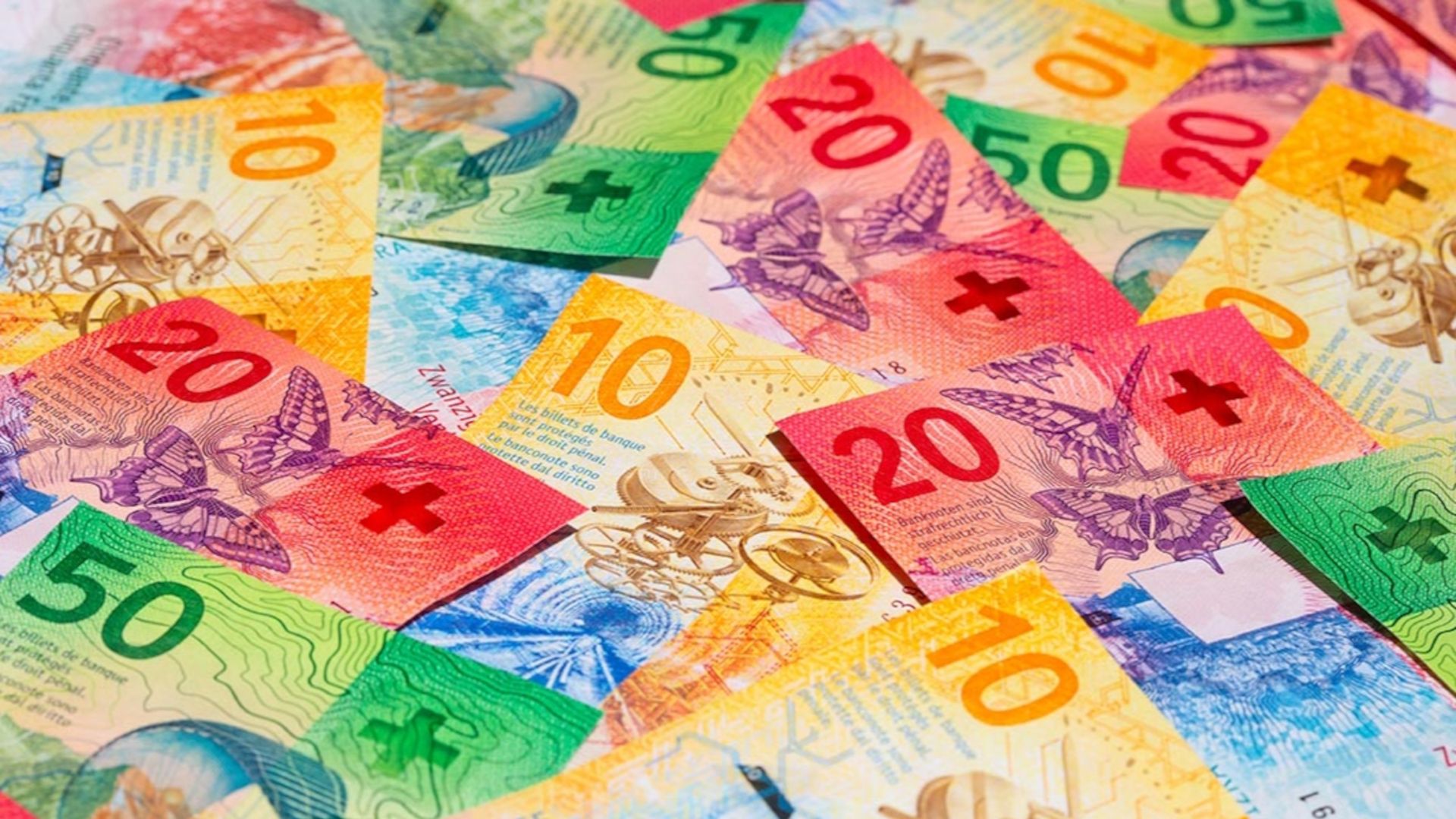 Verschiedene Schweizer Banknoten liegen auf und nebeneinander arrangiert. Zu sehen sind 10er Noten in Gelb, 20er Noten in Rot und 50er Noten in Grün, die zusammen eine bunte, unordentliche Geldansammlung bilden.