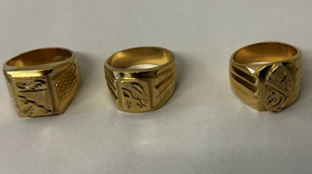 Goldfarbene Ringe mit unterschiedlichen Gravuren liegen nebeneinander auf einer hellen Unterlage. Die Ringe sind gefälscht und wirken massiv.