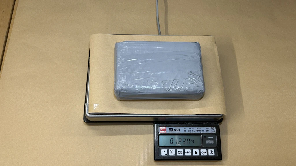 Ein in graues Klebeband eingepacktes Paket liegt auf einer Waage. Das Display der Waage zeigt ein Gewicht von 1,23 Kilogramm an. Das Paket wurde vermutlich von einer Behörde sichergestellt. 