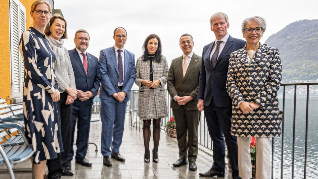 Mehrere Personen stehen anlässlich einer Vernissage nebeneinander auf einer Terrasse mit Blick auf einen See und lächeln in die Kamera. Im Hintergrund sind Berge und Wasser zu sehen.