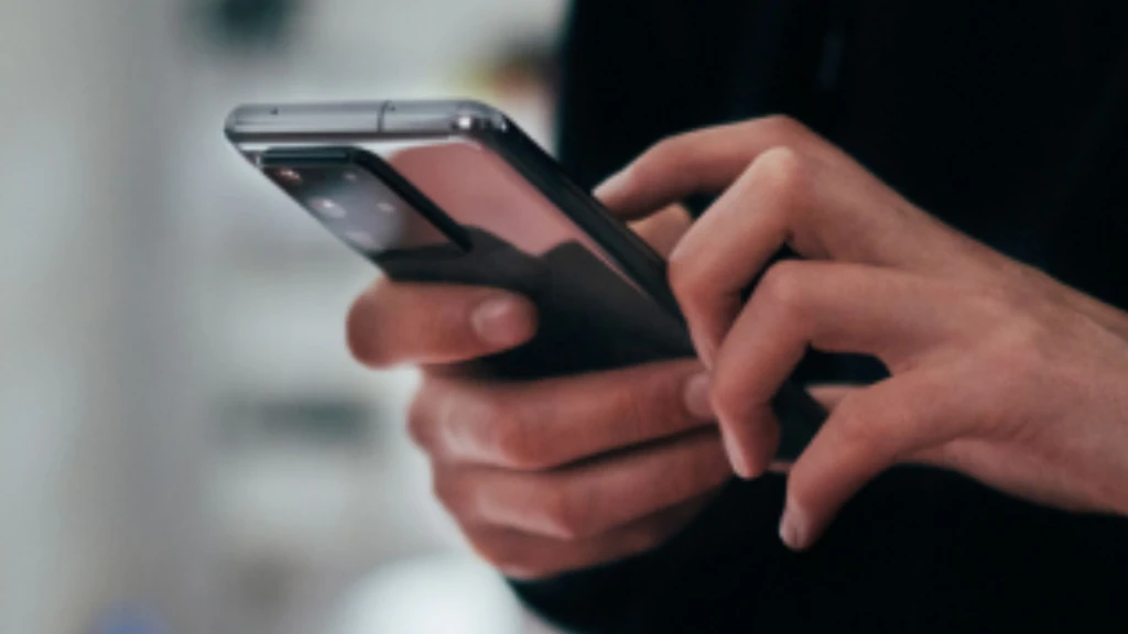 Eine Person hält ein Handy in der Hand und tippt etwas ein. Man sieht nur die Hände dieser Person