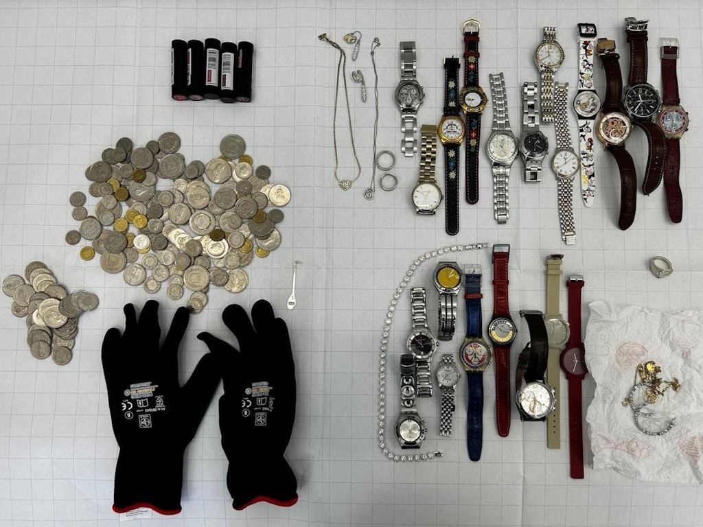 Eine Sammlung von sichergestellten Münzen, Uhren und Schmuckstücken auf einem Tisch. Die Gegenstände sind sorgfältig angeordnet und umfassen verschiedene Arten von Uhren und Münzen.