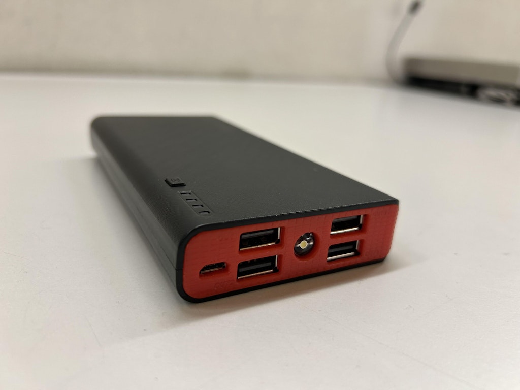 Eine schwarze und rote externe Powerbank mit mehreren USB-Anschlüssen liegt auf einem weissen Tisch.