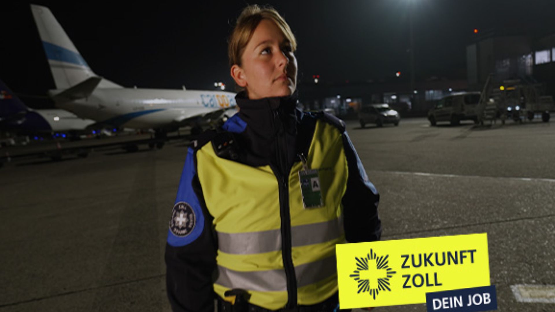 Eine Mitarbeiterin des Zolls am Flughafen vor einem Flugzeug bei Dunkelheit