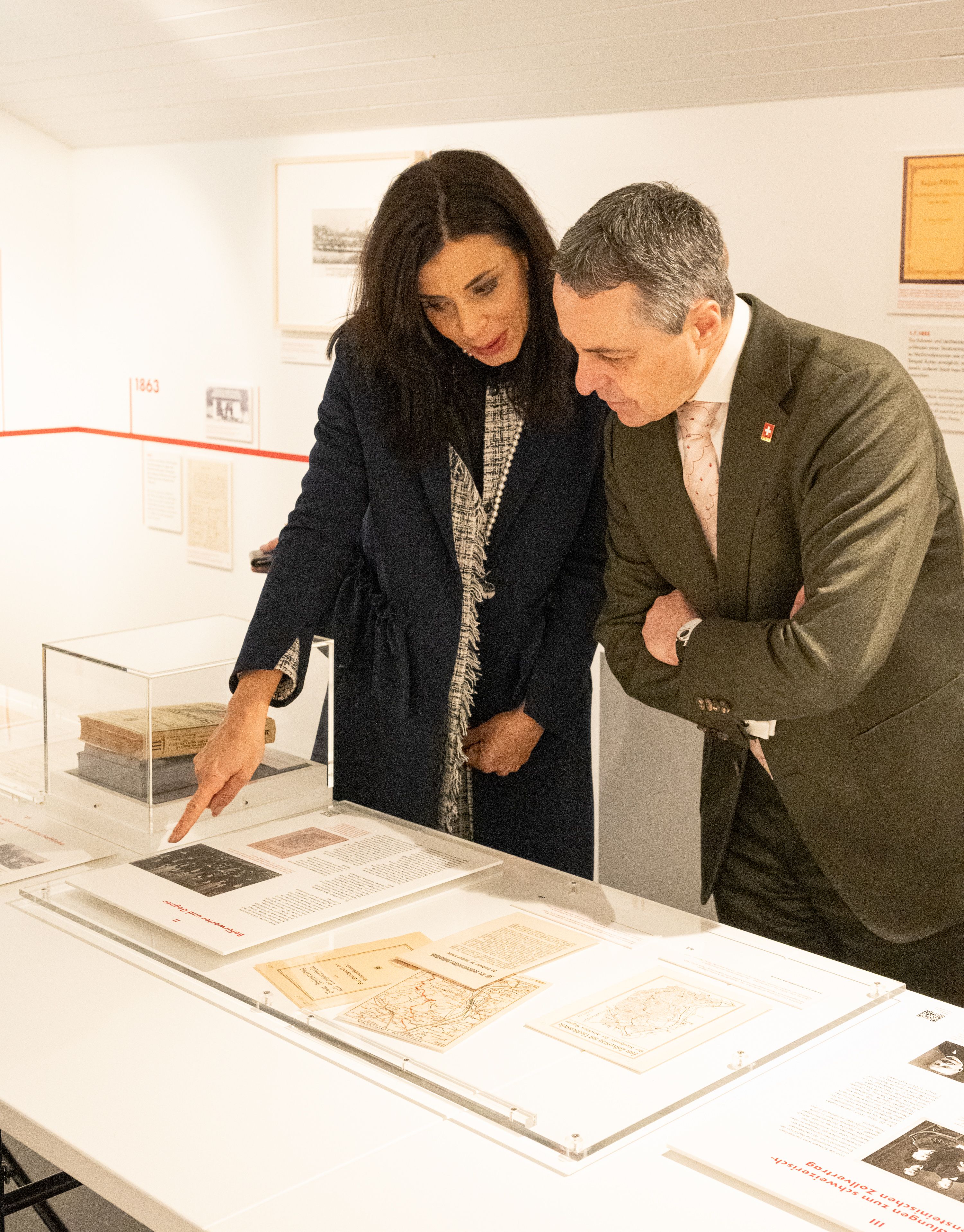 Zwei Personen betrachten Exponate in einer Ausstellung. Sie stehen vor einem Tisch mit Dokumenten und Karten.  