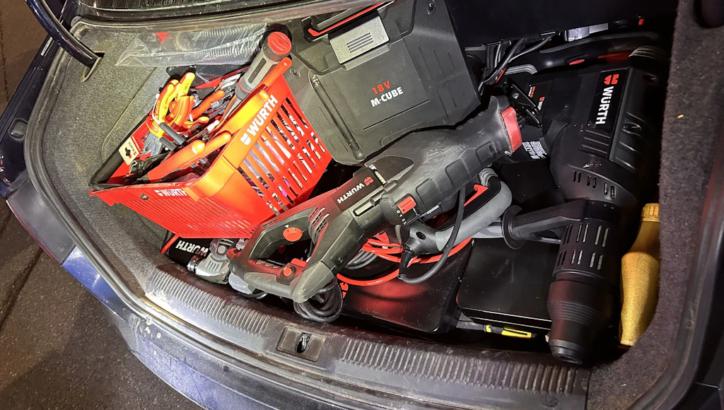 Im Kofferraum eines Autos befinden sich verschiedene Elektrowerkzeuge und Handwerkzeuge der Marke Würth. Die Werkzeuge sind ordentlich in einem roten Korb und daneben platziert. Die Szene ist gut beleuchtet und zeigt die Ausstattung für handwerkliche Arbeiten unterwegs.  