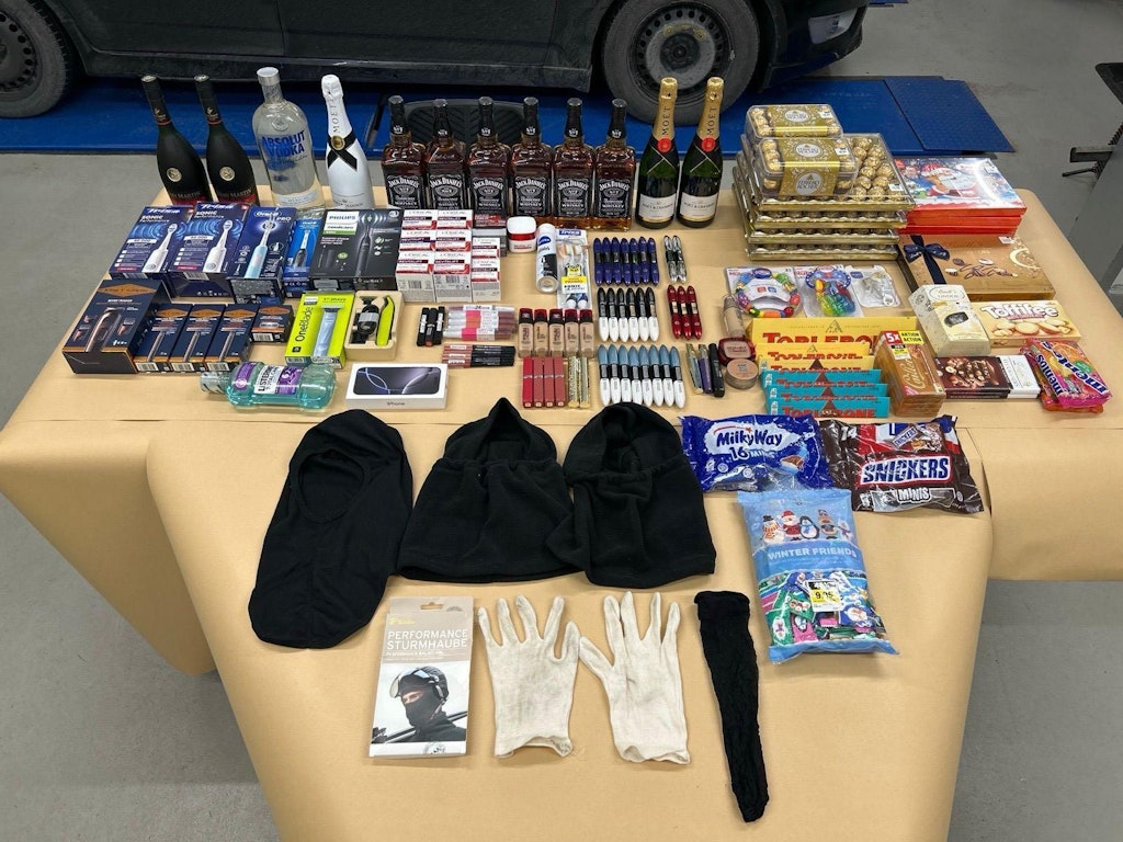Ein Tisch voller verschiedener Gegenstände, darunter Alkoholflaschen, Elektronik, Kosmetikartikel und Süßigkeiten. Auch Einbruchsutensilien wie Sturmhauben und Handschuhe sind zu sehen.