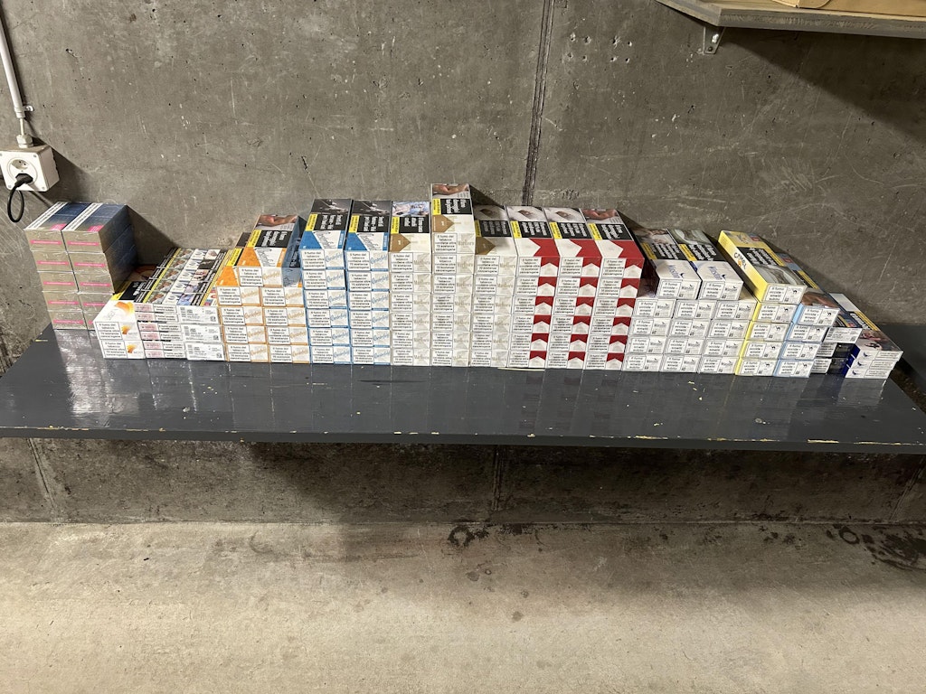 Mehrere Stapel von Zigarettenschachteln auf einem Tisch vor einer Betonwand. Die Packungen sind in verschiedenen Farben und Mustern sortiert.