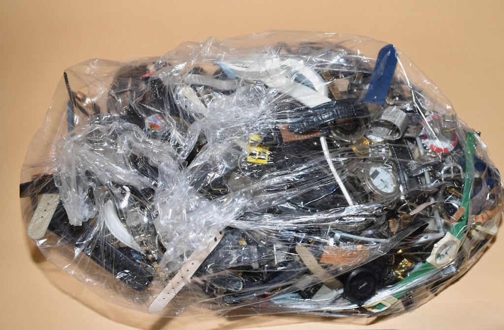 Eine Sammlung von Uhren, die in Plastikfolie eingewickelt sind. Die Uhren scheinen mutmasslich gestohlen zu sein. Verschiedene Armbänder und Zifferblätter sind sichtbar.