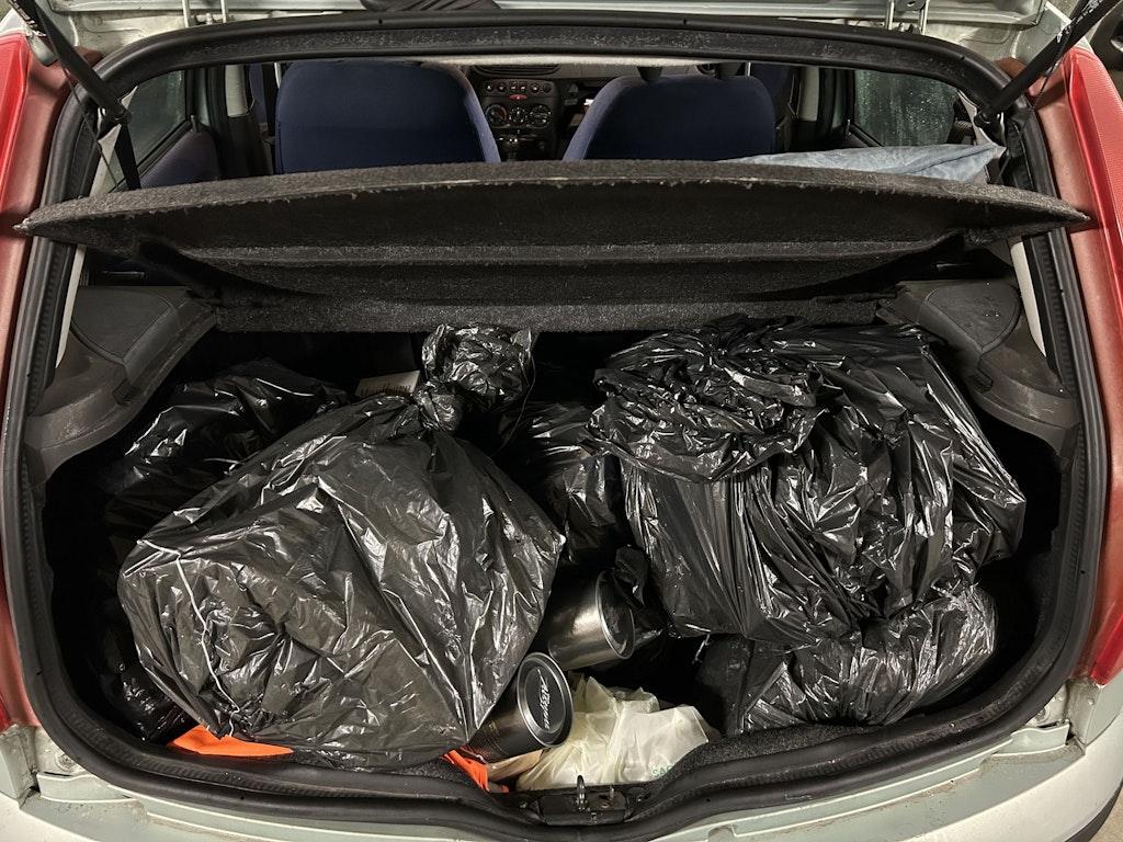 Der Kofferraum eines Autos ist mit mehreren schwarzen Müllsäcken gefüllt. Diese enthalten geschmuggelte Zigaretten. Die Szene deutet auf einen Schmuggelversuch hin.