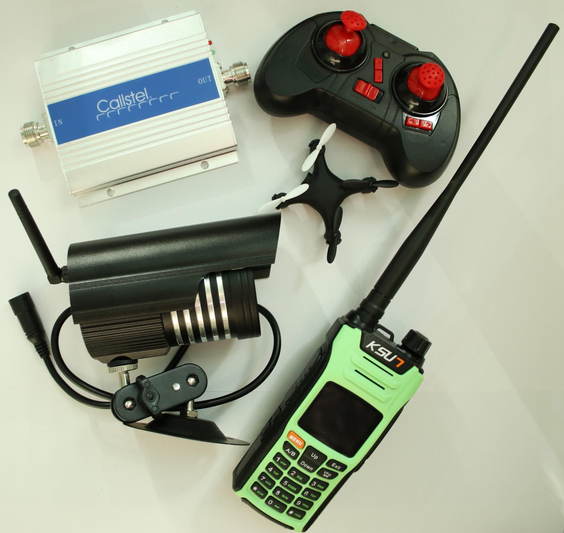 Verschiedene Kommunikationsgeräte auf einer Oberfläche, darunter ein Walkie-Talkie, eine Kamera, ein Signalverstärker und eine Fernbedienung.