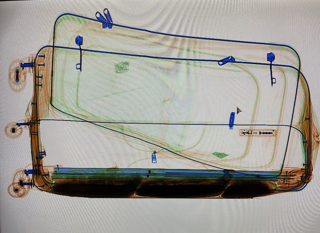 Ein Röntgenbild zeigt einen Koffer mit einem doppelten Boden. Die Struktur des Koffers ist deutlich zu erkennen, einschliesslich der Räder und Griffe.