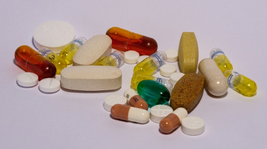 Verschiedene Tabletten und Kapseln in unterschiedlichen Farben und Formen liegen auf einer weissen Oberfläche. Die Darstellung zeigt eine Auswahl gängiger Medikamente und Nahrungsergänzungsmittel.