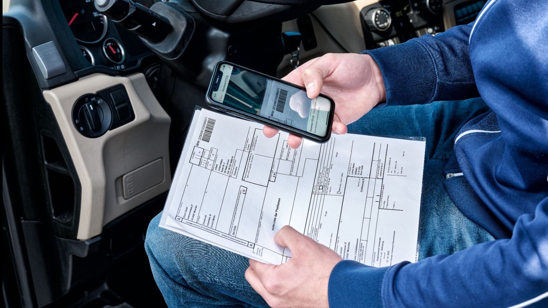 A person sits in a car and scans a document with a smartphone. The focus is on digitally capturing paper documents.  