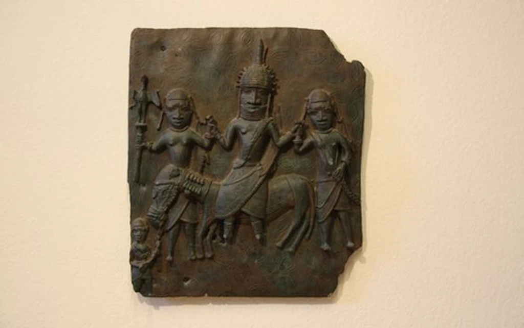 An ancient Benin bronze relief depicting three figures, including one on a horse. The figures are detailed and artistically crafted.