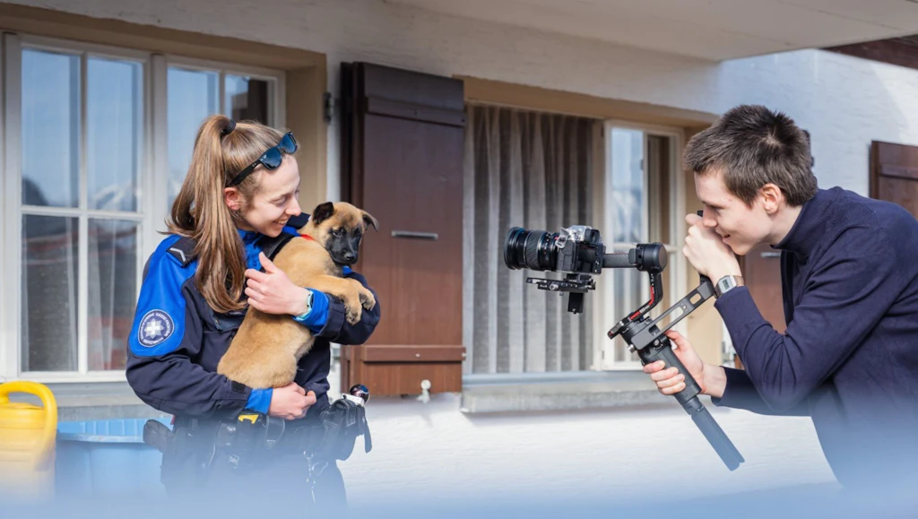 One woman is holding a puppy while a photographer takes their picture with a camera.