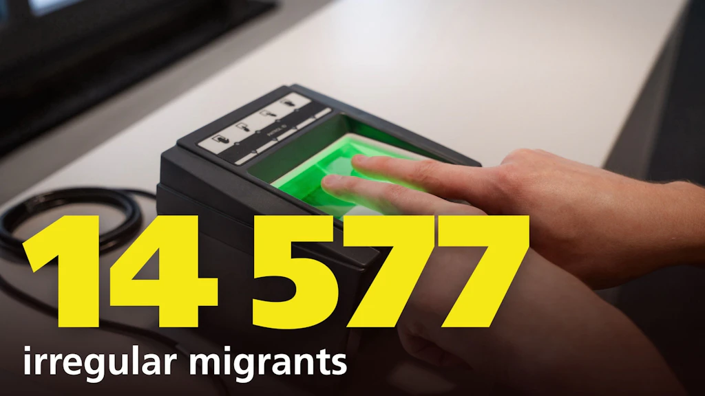 A hand is placed on a fingerprint scanner, with the number 14,577 and the text "irregular migrants" in the foreground. The image highlights the registration of irregular entries.