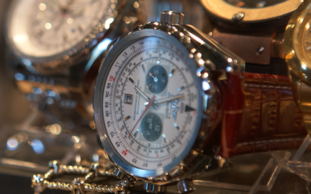 A close-up of a watch with a brown leather strap in an exhibition. The watch has a silver case and multiple dials.