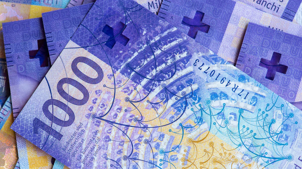 Several Swiss 1000-franc banknotes are stacked together. The notes are purple and display security features and the Swiss cross.