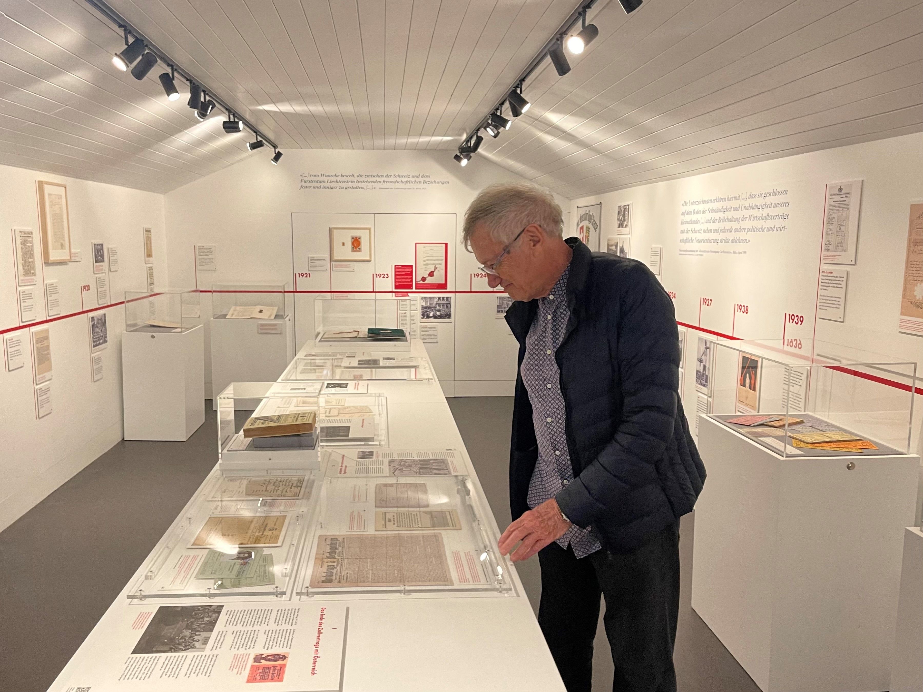 Un homme examine des objets dans une exposition au musée douanier. Les murs sont décorés de documents et d'images historiques.  