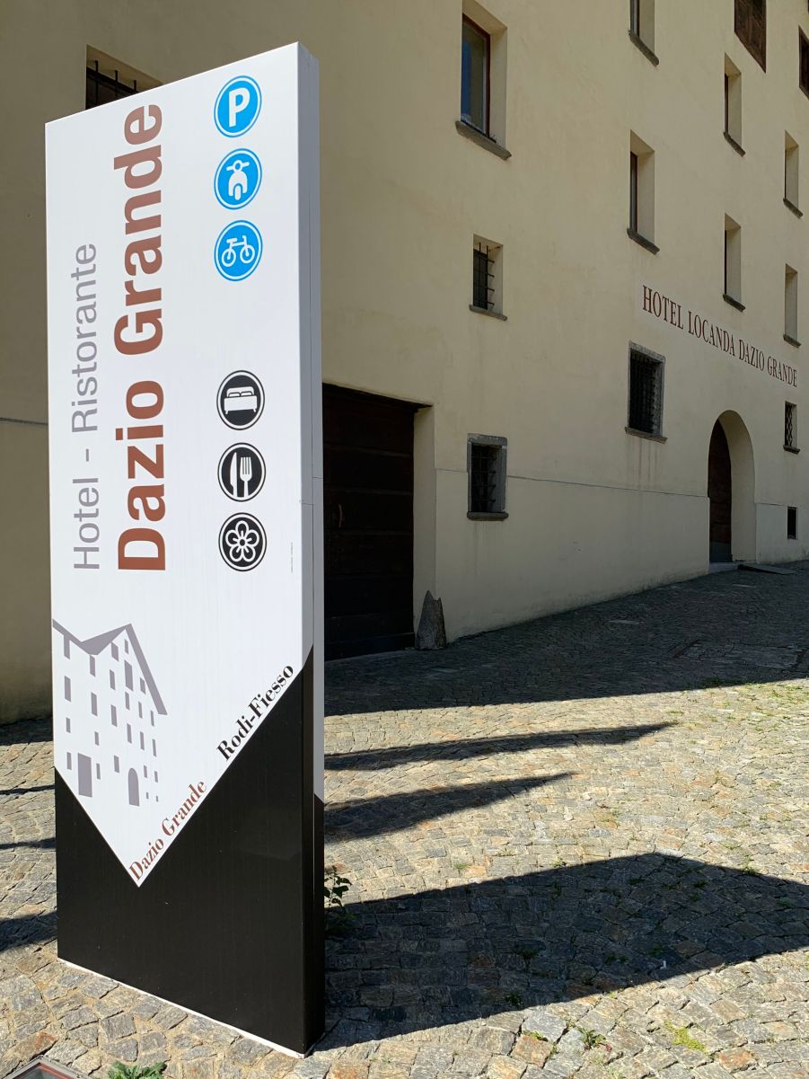 Un grand bâtiment traditionnel avec des drapeaux suisses et un panneau indiquant "Hôtel Locanda Dazio Grande" devant une montagne boisée.