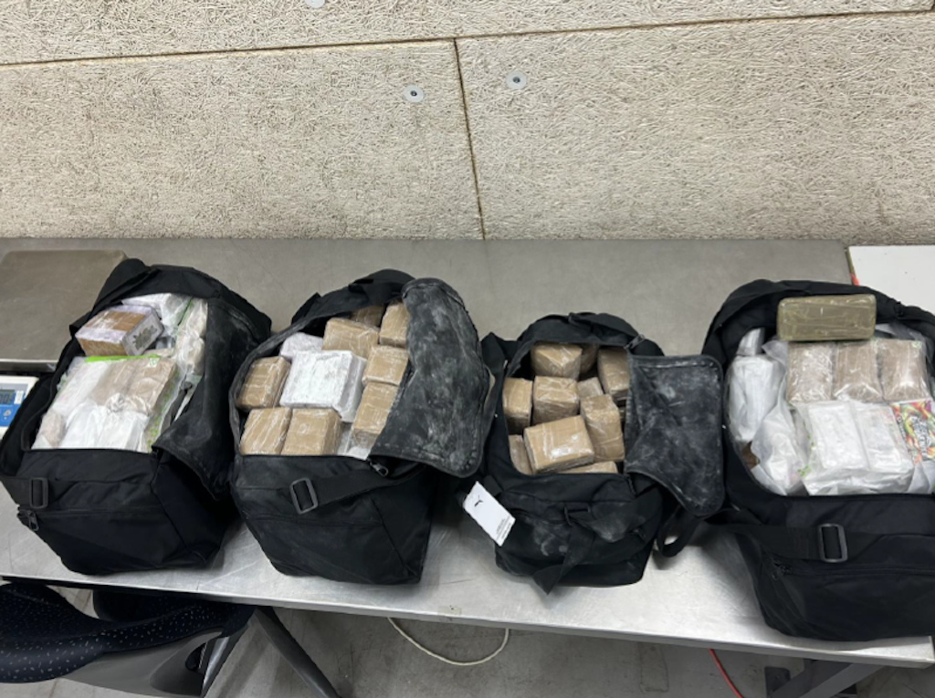 Quatre sacs noirs sur une table, remplis de paquets emballés dans du plastique. Ils ont été découverts dans une cachette.