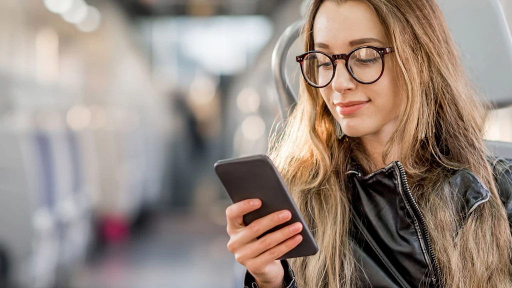 Jeune femme assise dans un train et regardant son smartphone