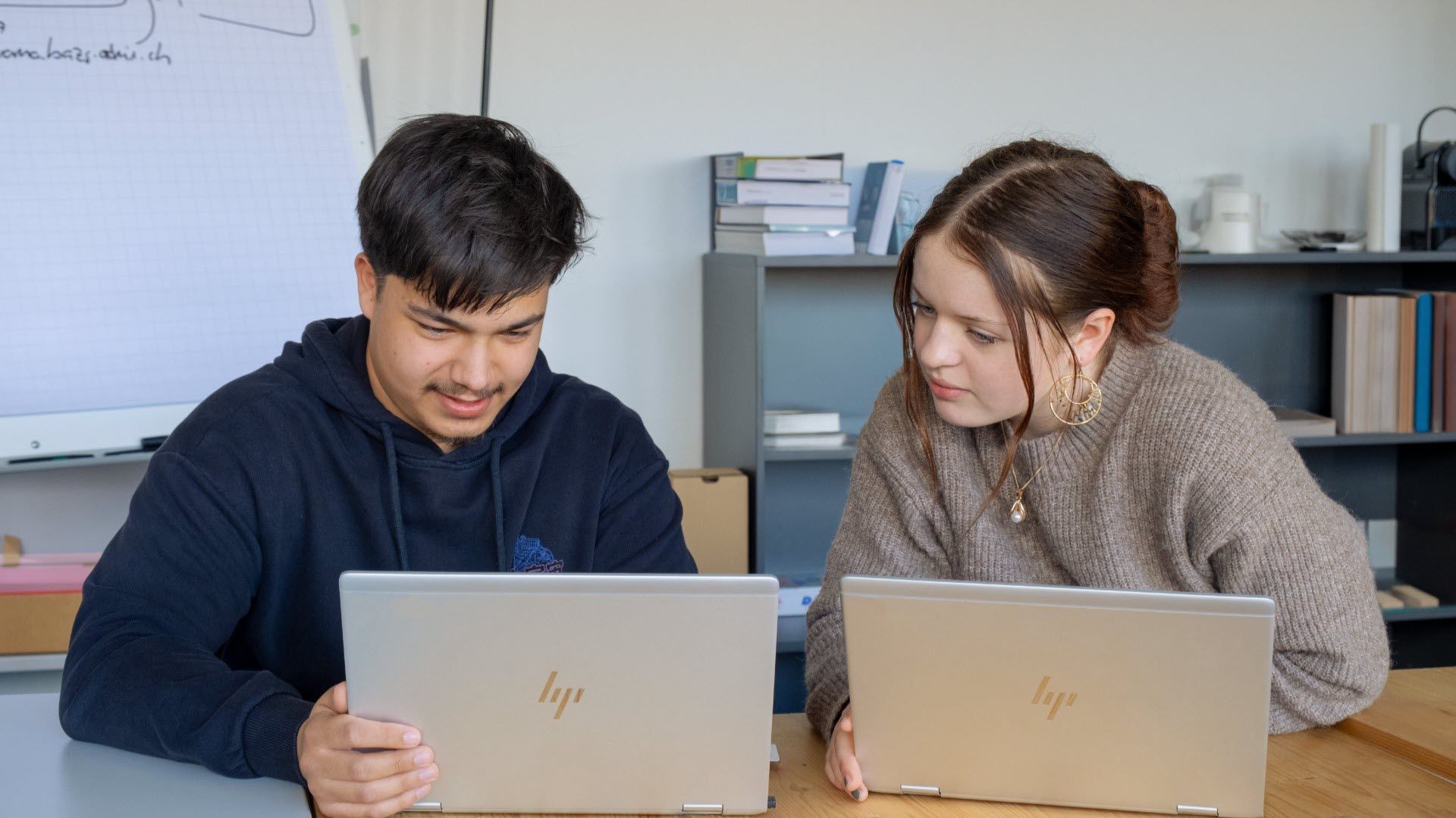 Deux personnes travaillent ensemble sur des ordinateurs portables dans un bureau. Elles semblent concentrées et discutent peut-être d'un projet.