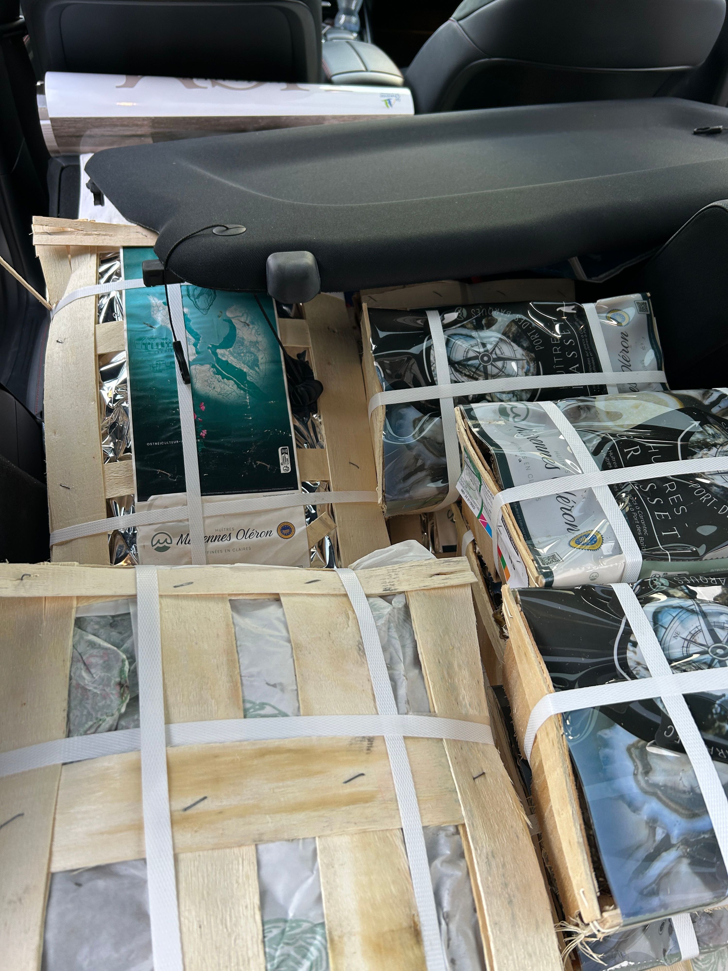 Plusieurs caisses d'huîtres déclarées impropres à la consommation sont entreposées dans un véhicule. Les caisses sont sécurisées avec des bandes blanches.