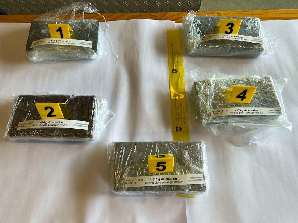 Cinq blocs de cocaïne emballés dans du plastique, numérotés de 1 à 5, sont posés sur une table. Chaque bloc pèse environ un kilogramme. Les blocs sont marqués avec des étiquettes jaunes numérotées.