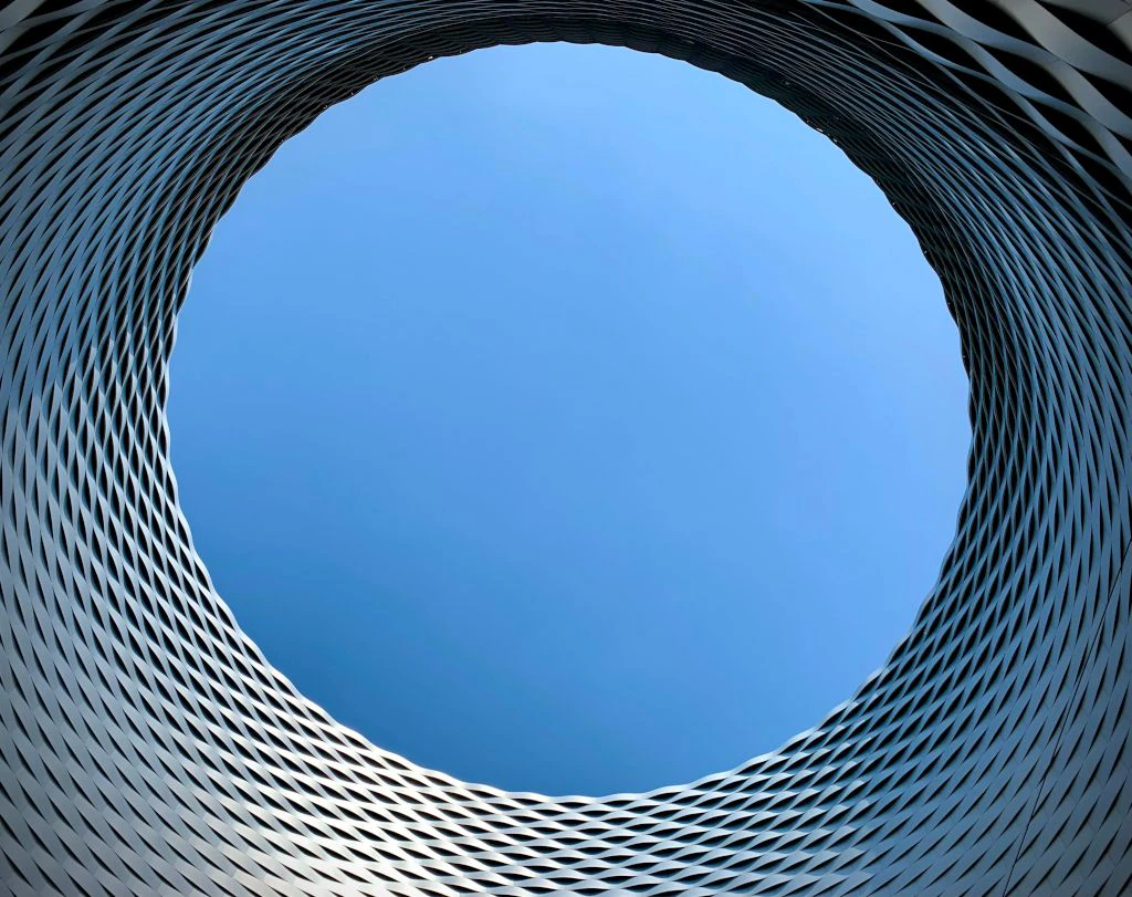 Vue à travers une ouverture circulaire dans une façade métallique moderne vers le ciel bleu. La structure forme un motif dynamique en spirale.