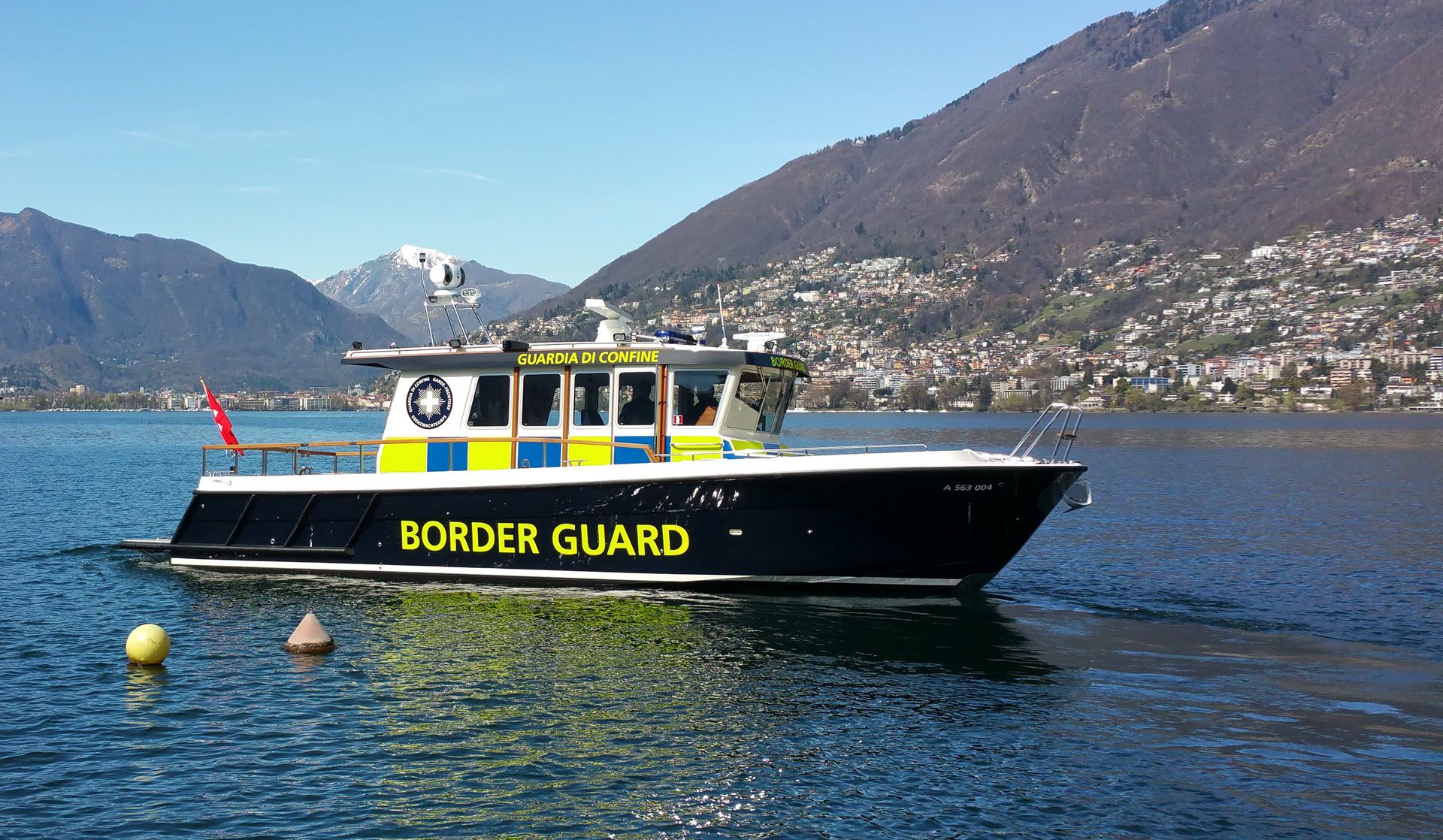 Un bateau de la garde frontière navigue sur un lac avec des montagnes en arrière-plan. 